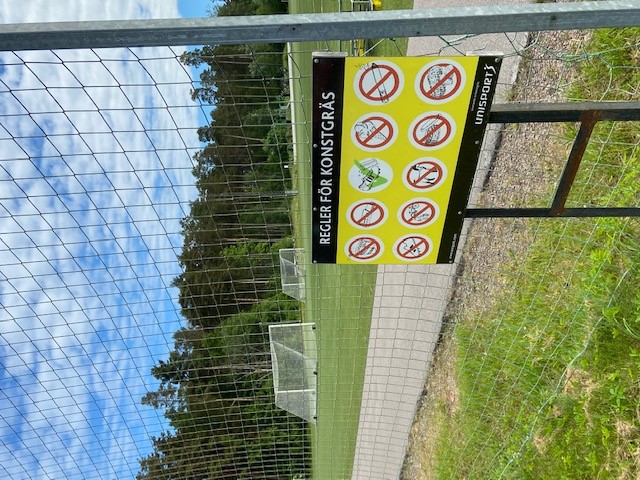 Informationsskylt i förgrunden med konstgräsplanen i bakgrunden