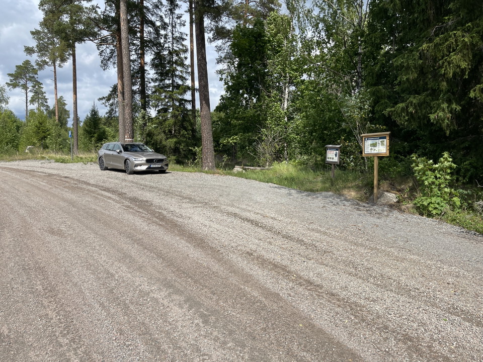 Bil parkerad på en grusad yta. En p-skylt och informationstavlor.