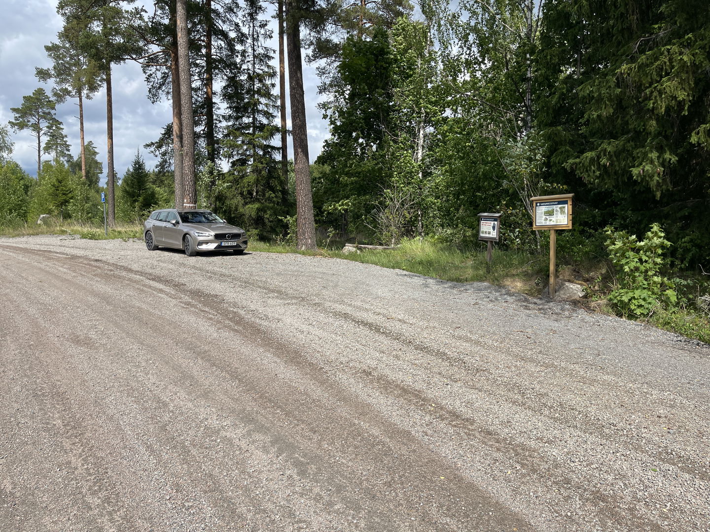 Bil parkerad på en grusad yta. En p-skylt och informationstavlor.