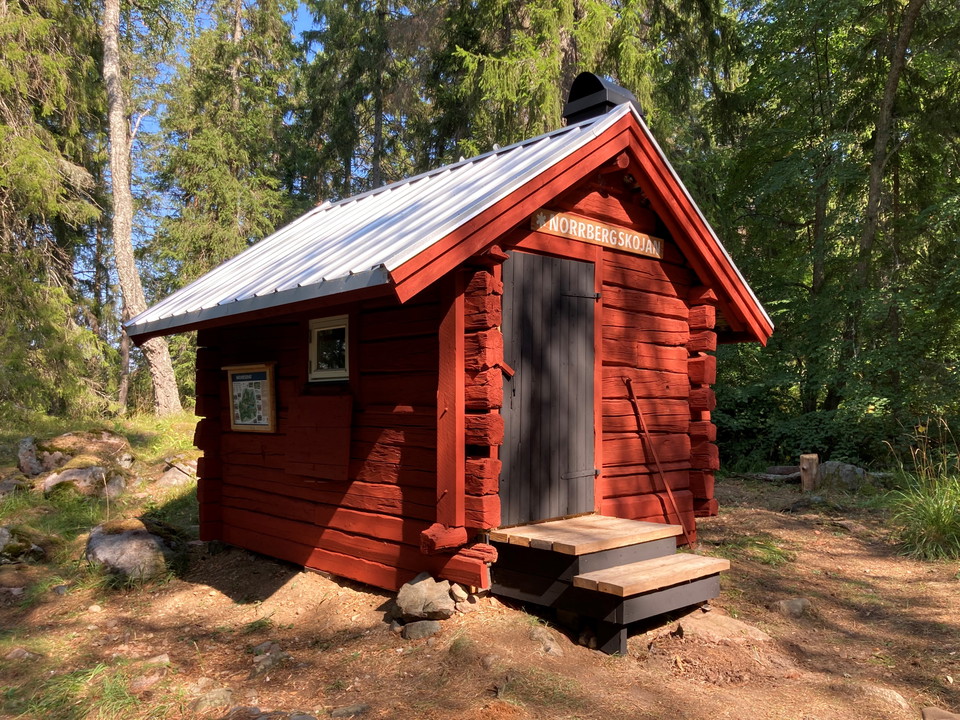 En liten röd stuga i korsvirke med plåttak.