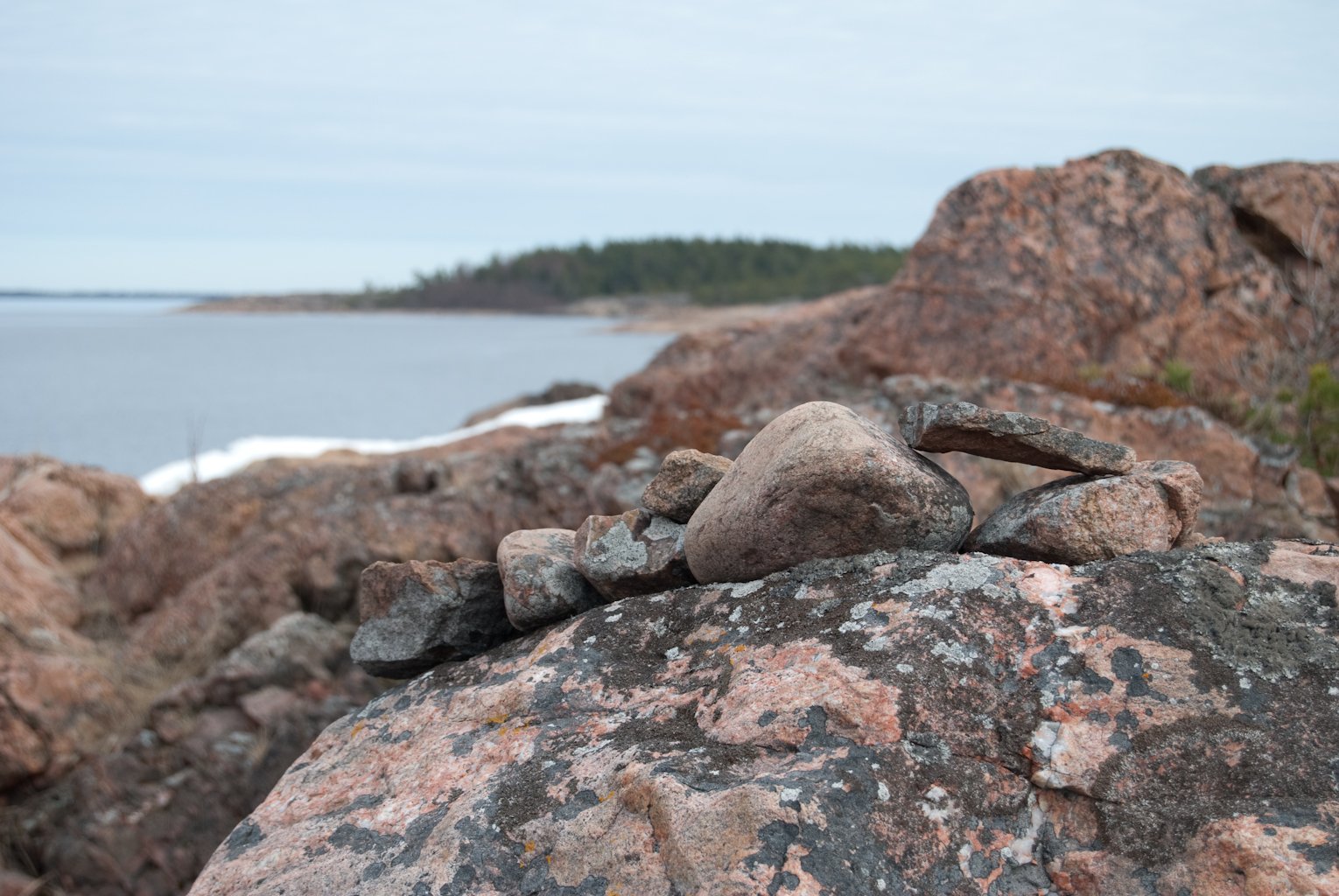 Närbild på stenar upplagda på rad ovanpå en klippa. I bakgrunden skymtar havet fram. 