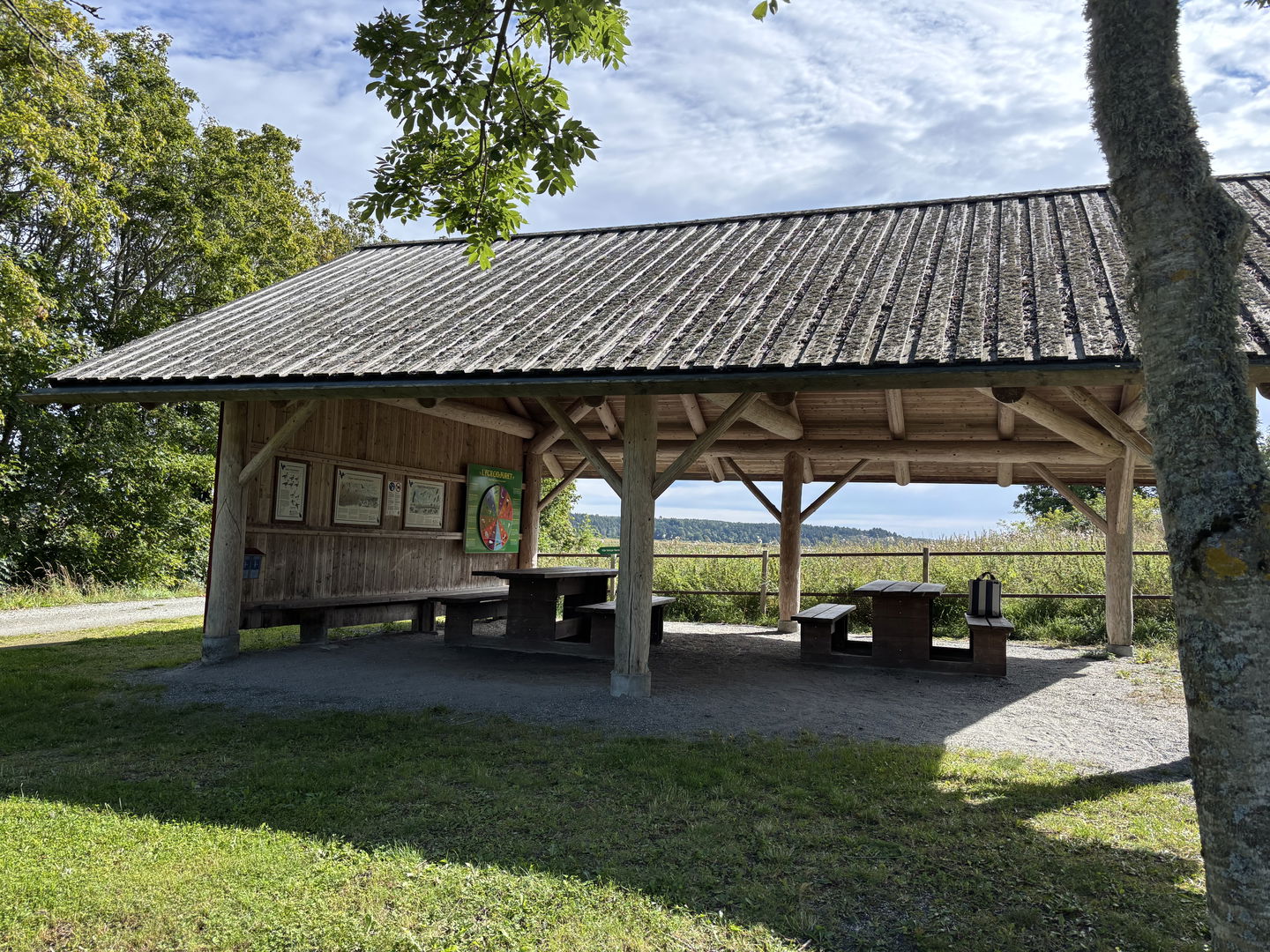 Ett stort träfärgat tak som bärs upp av stolpar. Under taket står flera rastbord. 
