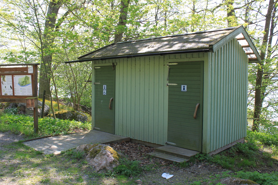 En byggnad med torrtoaletter står nära stranden. En ramp leder upp till ena toadörren och en kort trappa leder upp till den andra dörren.