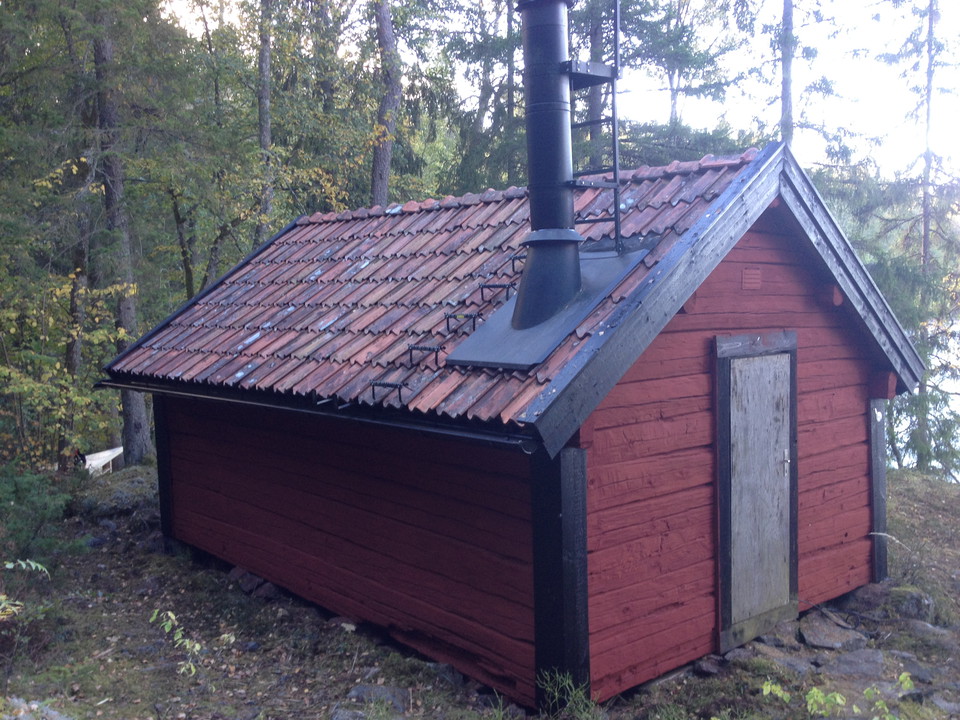 En liten stuga med hög skorsten står i skogen. 