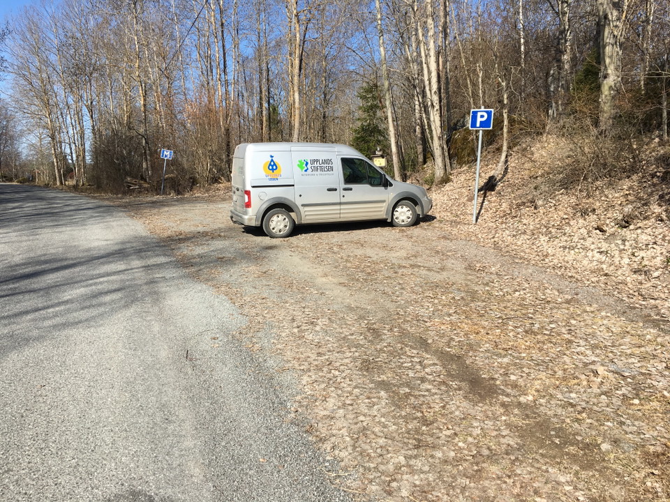 En skåpbil är parkerad på en avlång grusad parkeringsplats intill en bilväg.