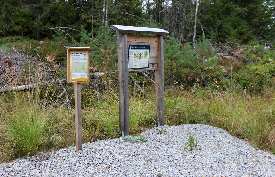 Två skyltar vid uppgrusad parkeringsyta.