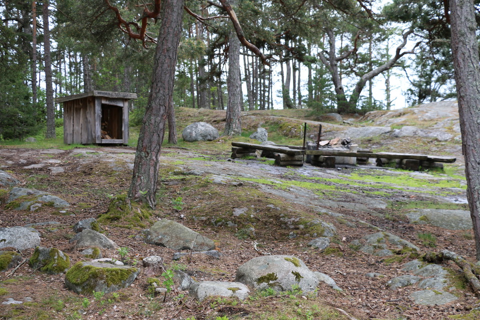 Rastplats på klippor med eldstad, vedförråd och bänkar.