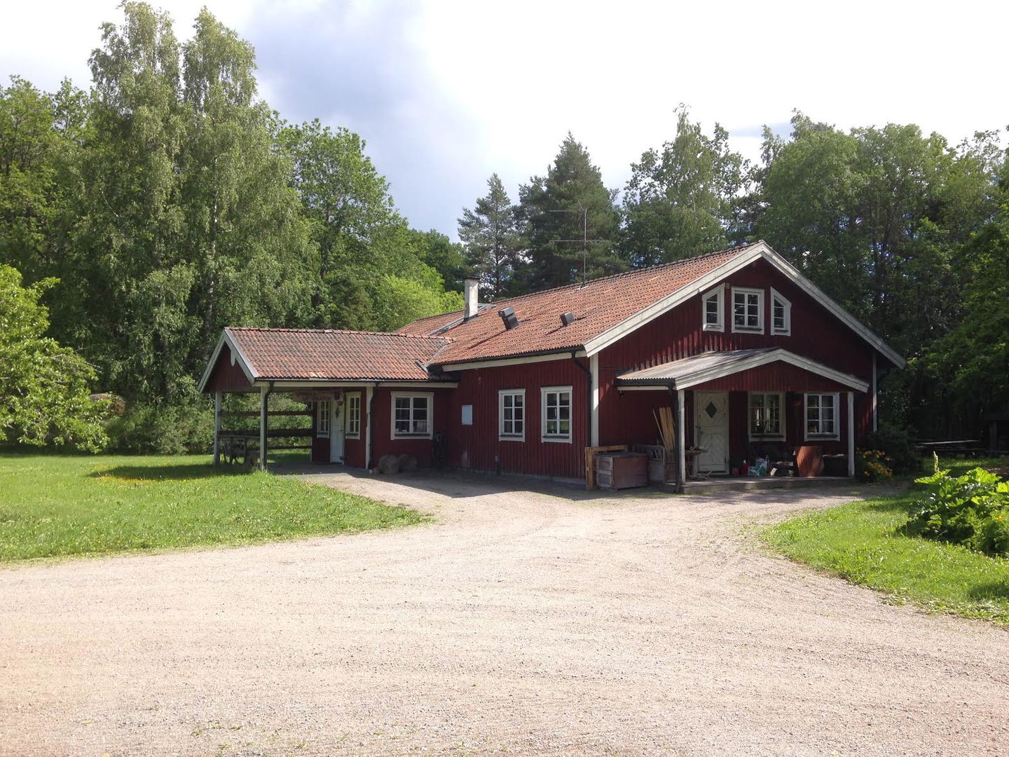 En grusväg leder fram till en byggnad med två ingångar. Bakom byggnaden är det skog.