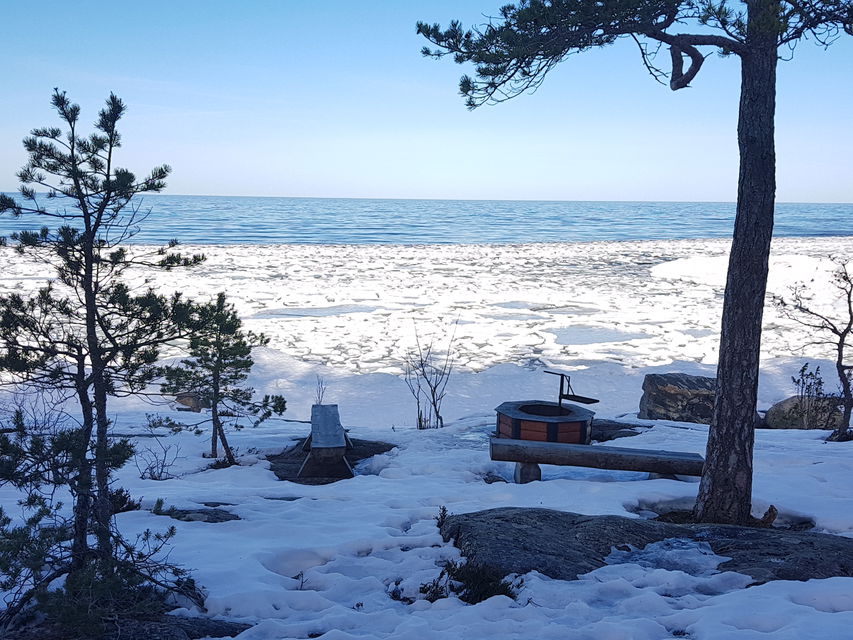En grillplats på en stenhäll vid havet. Både hällen och grillplatsen är täckta av snö.