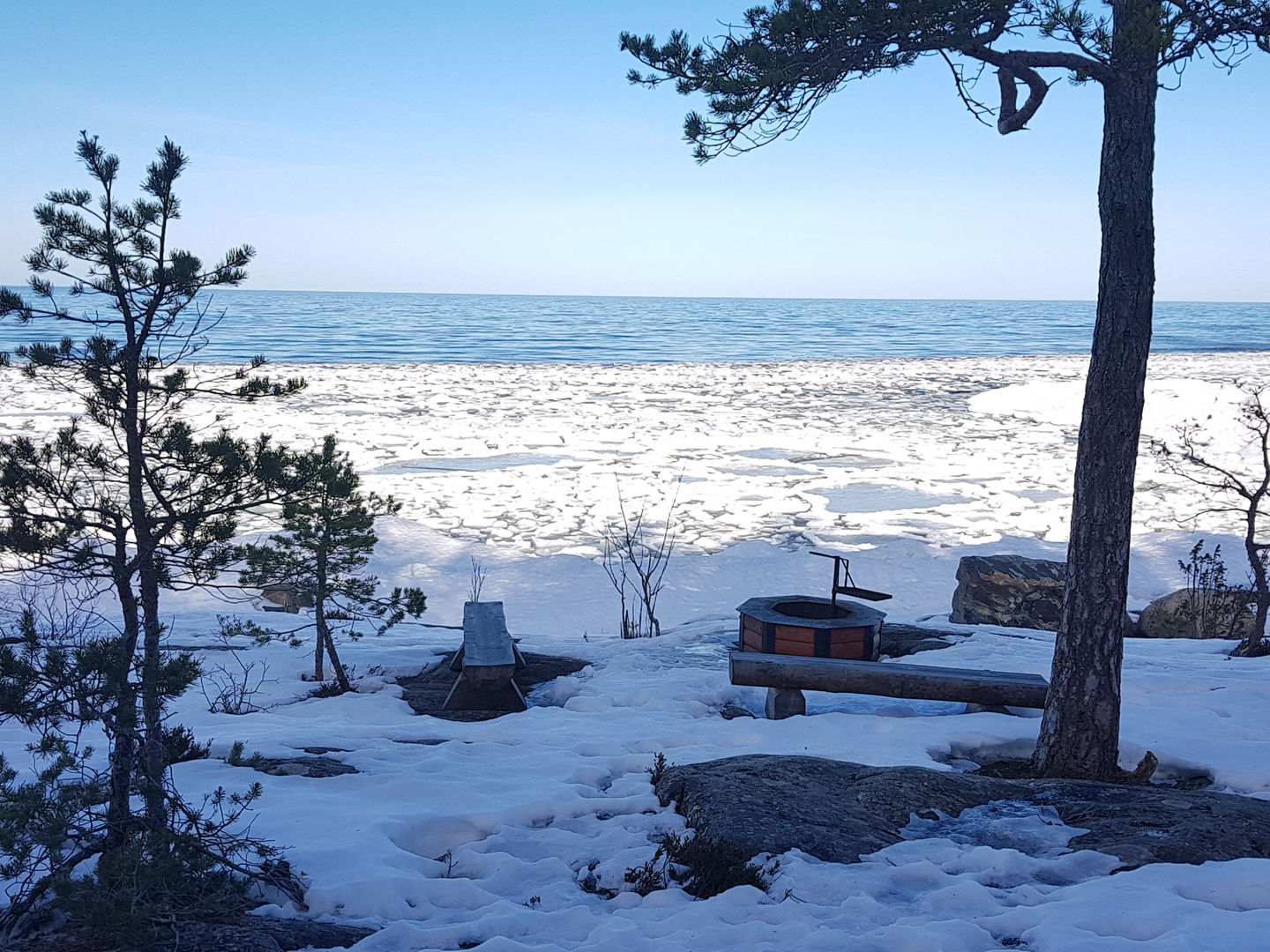 En grillplats på en stenhäll vid havet. Både hällen och grillplatsen är täckta av snö.