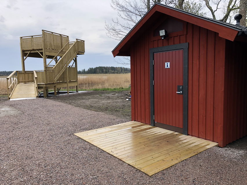 Röd byggnad med träramp framför och fågeltorn i bakgrunden