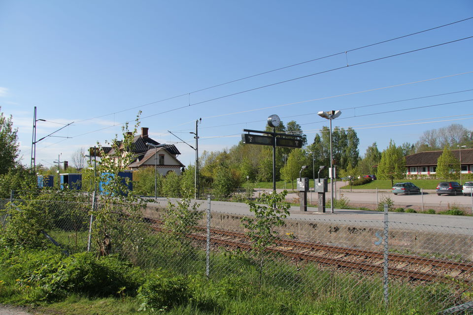 Tågstationen fotad från andra sidan rälsen med ett staket emellan.