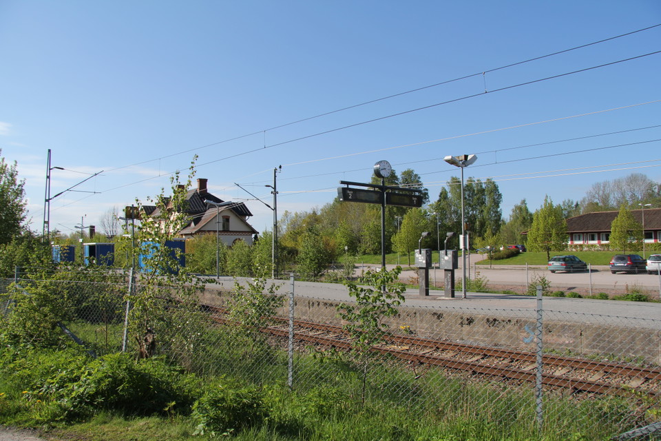 Tågstationen fotad från andra sidan rälsen med ett staket emellan.