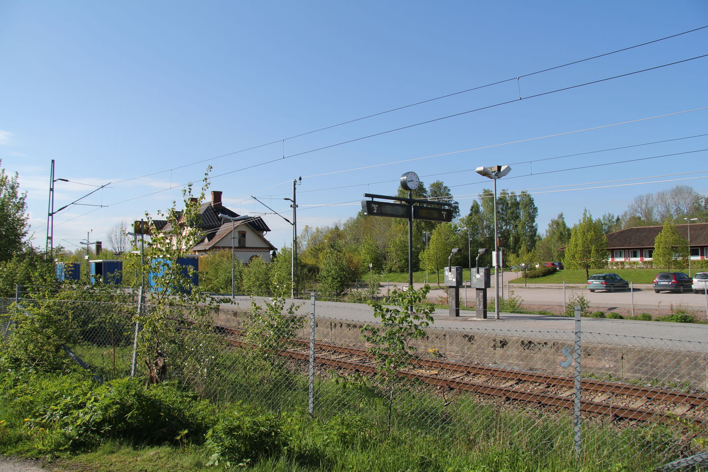 Tågstationen fotad från andra sidan rälsen med ett staket emellan.