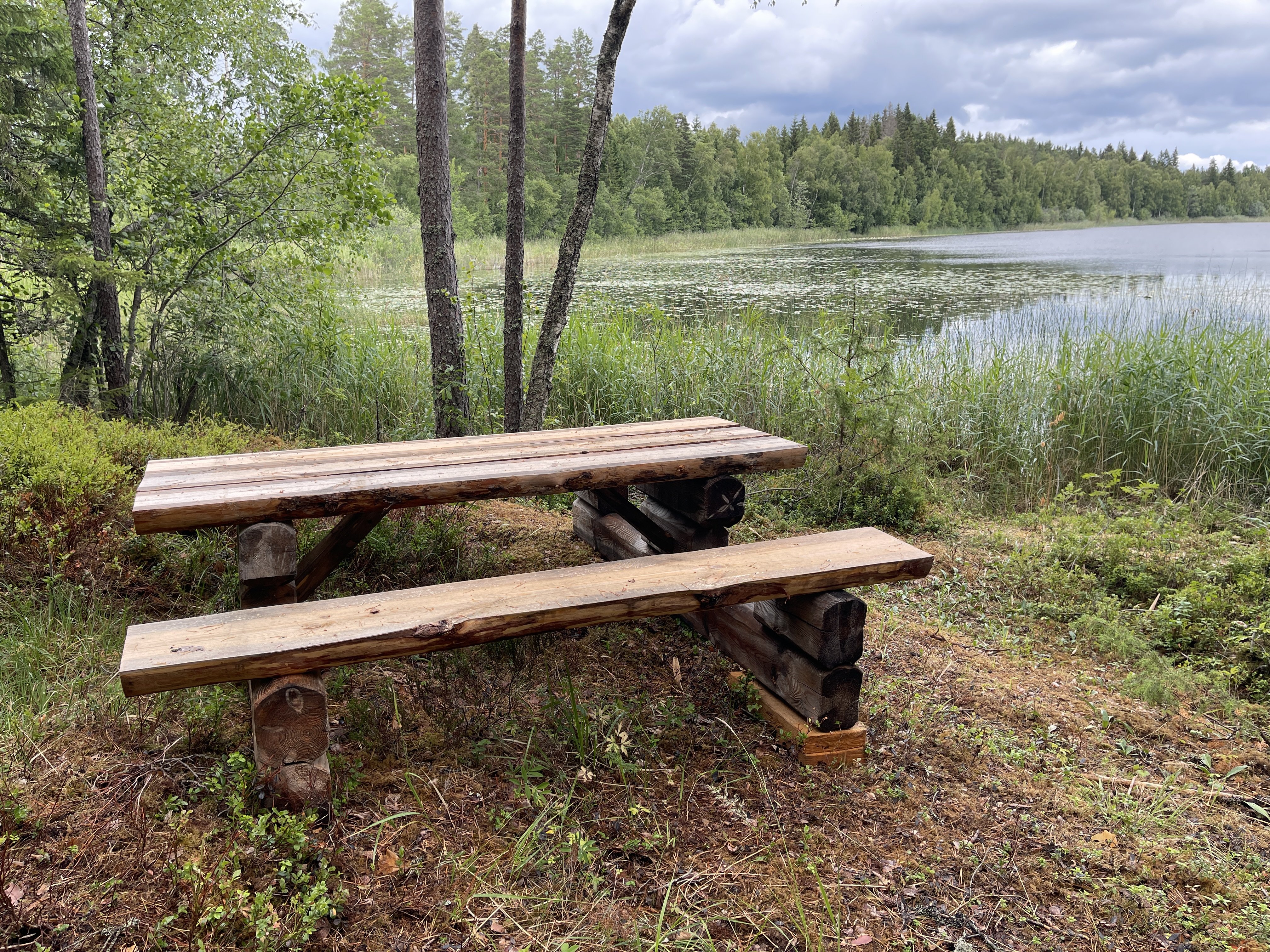 Picknickbord med bänkar och utsikt över sjö.
