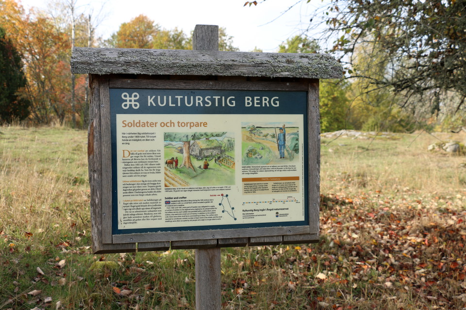 Informationstavla på ett träställ i höstlandskap.