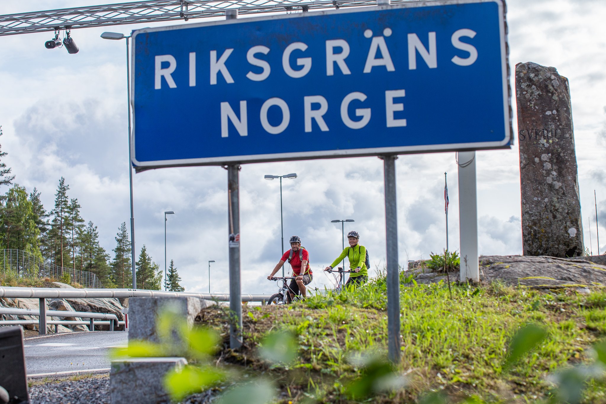 Skylt Riksgränsen Norge och två cyklister