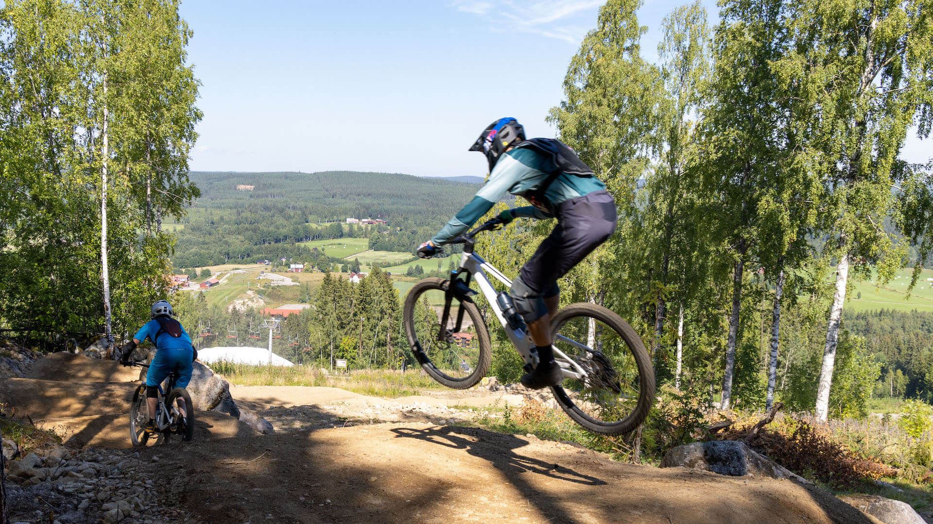 Cyklist som hoppar på grusväg med en dal som bakgrund