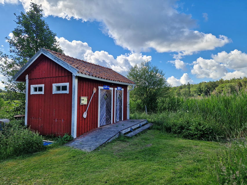 Röd liten byggnad med två dörrar. På en väggen hänger en paddel.