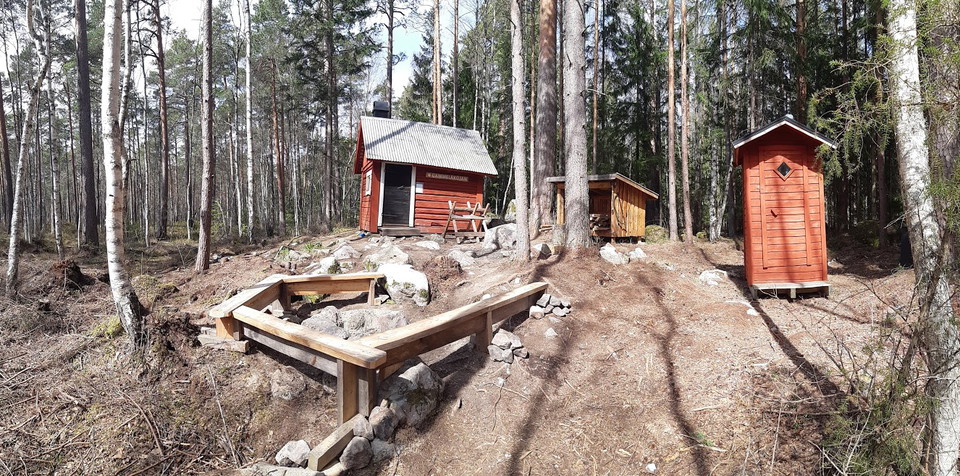 Röd stuga med vedförråd, utedass och grillplats med omgivande bänkar
