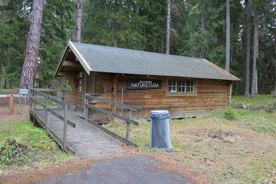 En liten trästuga med en bred ramp upp till entrén. Rampen har handräcken och bredvid står en soptunna.