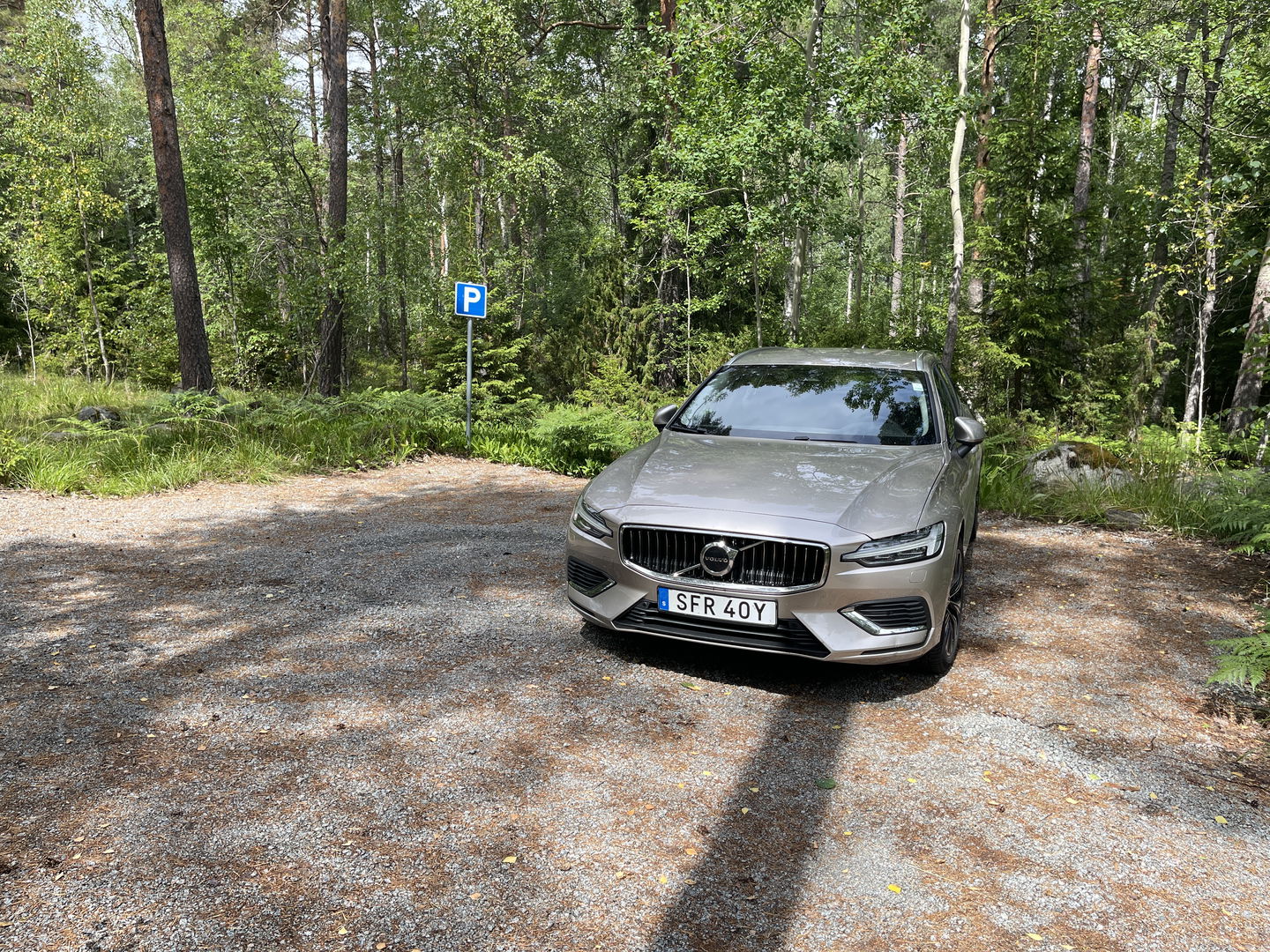 Bil parkerad på en grusad yta. En p-skylt.