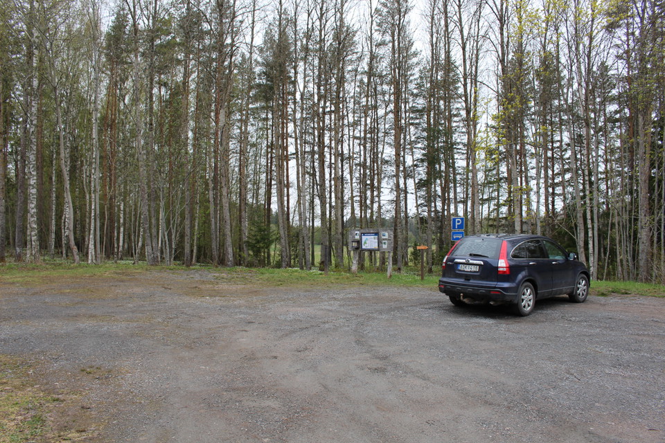 En bil står på en rymlig, grusad parkeringsplats. Vid platsen finns en informationstavla.