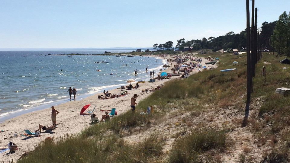 En sandstrand med folk som solar och badar.