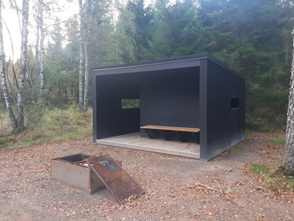 Ett vindskydd med skog i bakgrunden.