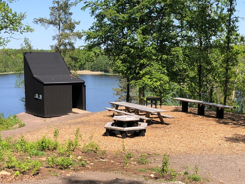Ett vindskydd med bänkbord och med skog och sjö i bakgrunden.
