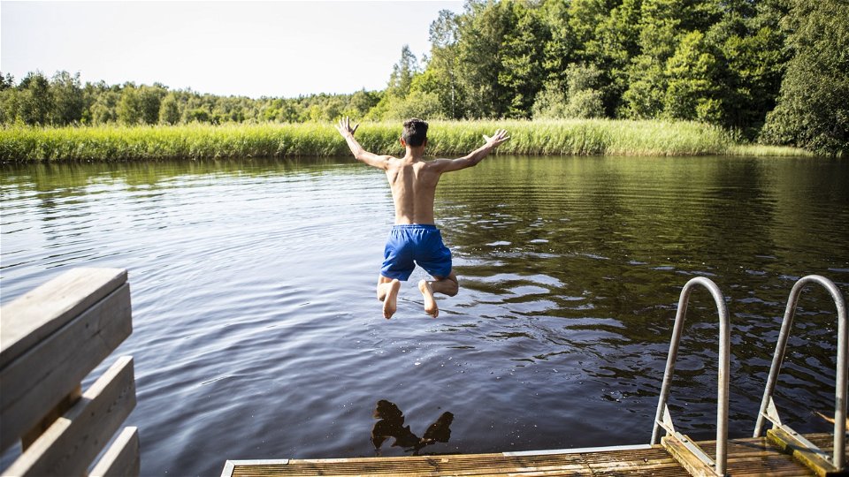 En pojke hoppar i vattnet från en brygga