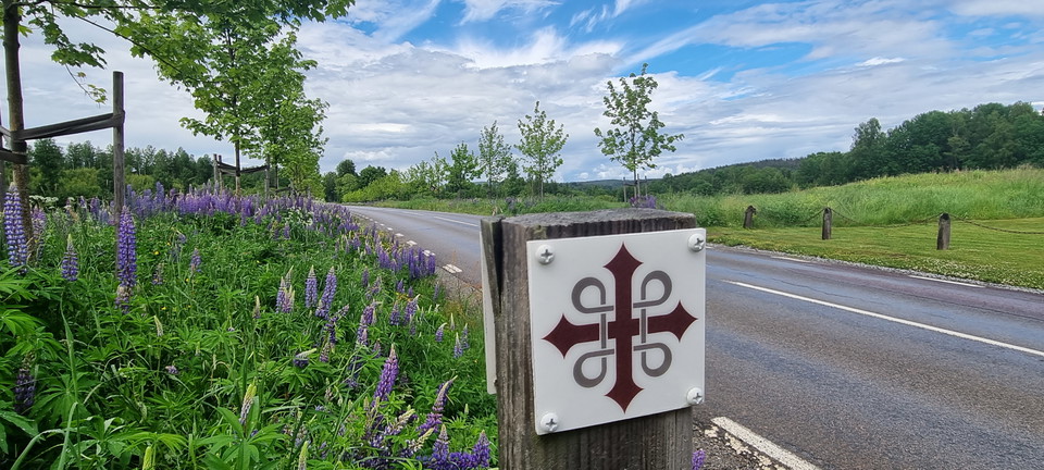 St Olofskorset på trästolpe längs vägen.