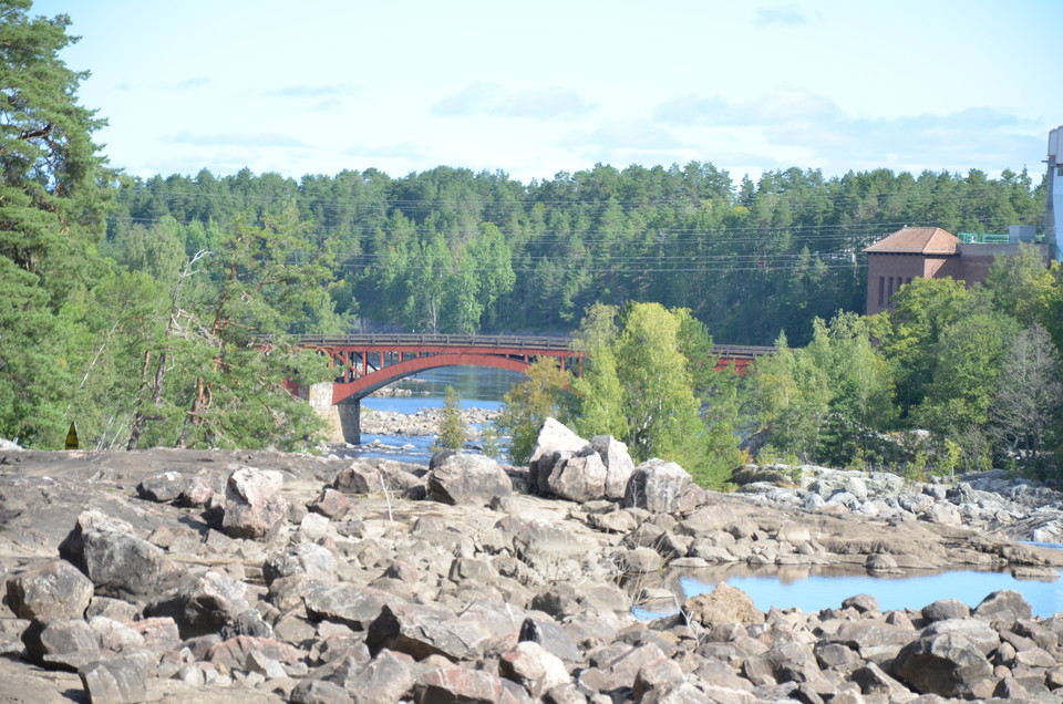 I förgrunden kala stenblock. Bakom dessa vatten och en röd bro.