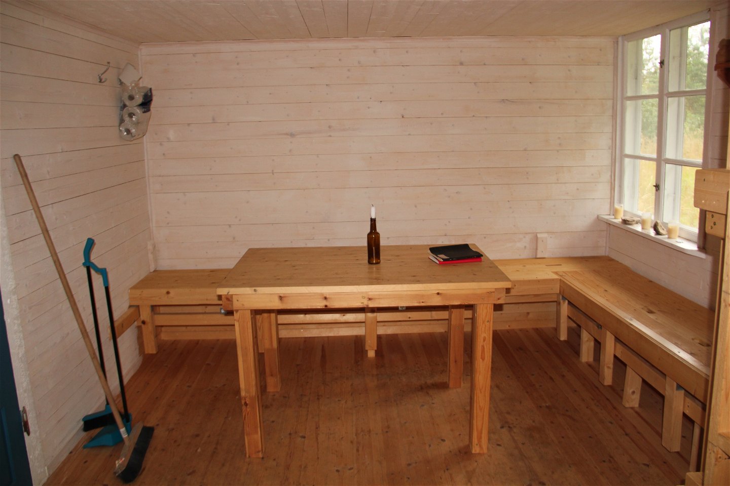 Insidan av stugan med väggfasta bänkar och ett bord.