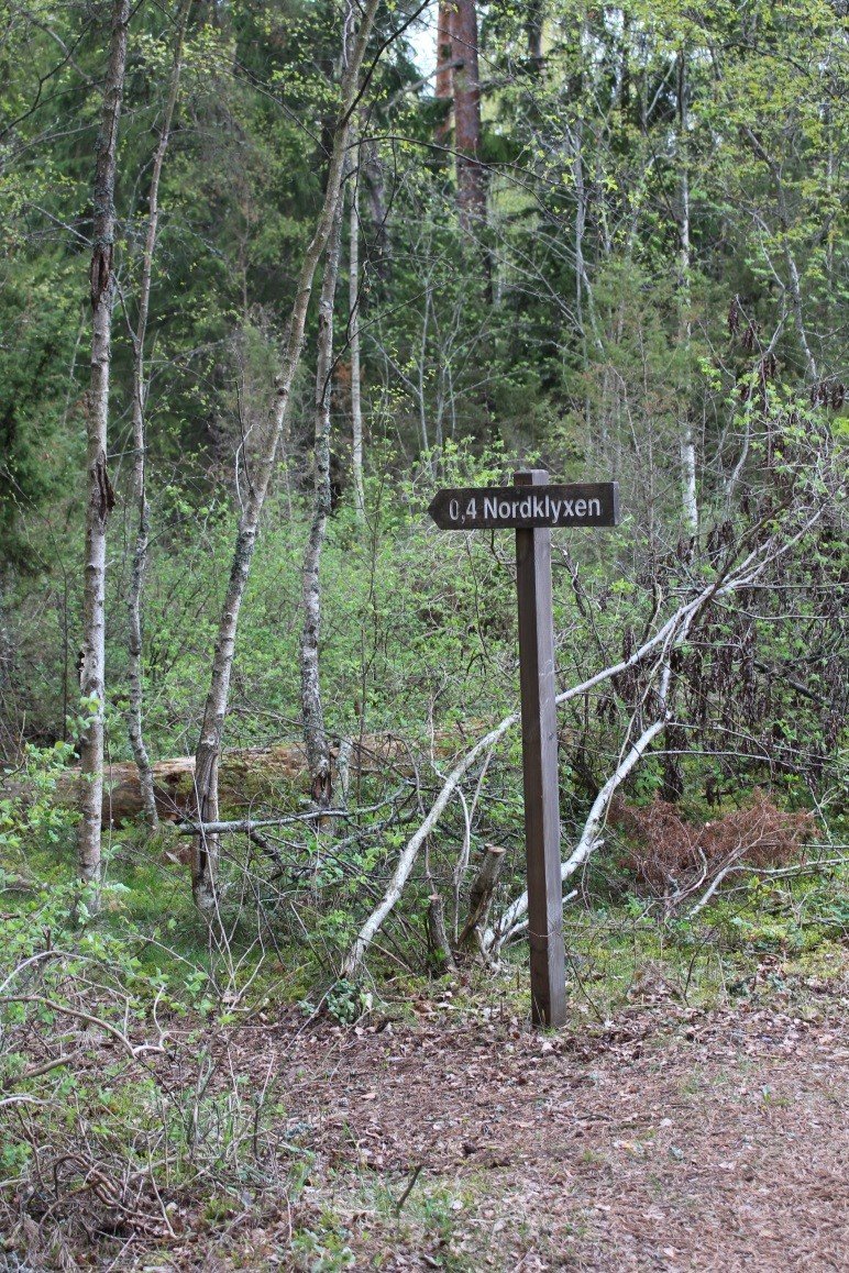 I skogen står en skylt med en pil som pekar åt vänster. På pilen står det 0,4 Nordklyxen.