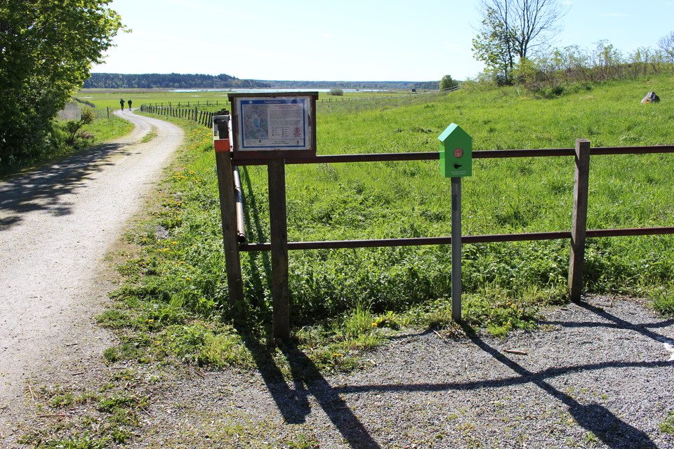 En bred grusad stig går längs med en stängslad gräshage. Vid hagen står en informationstavla.