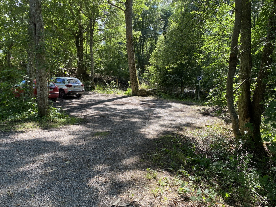Två bilar står parkerade på en liten grusad parkering. Runtom parkeringen finns många träd.