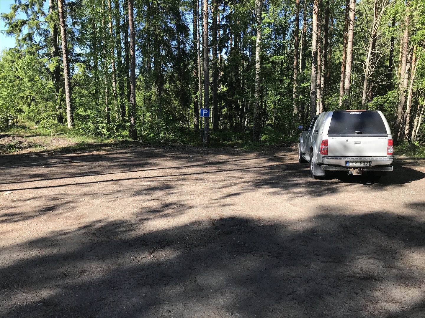 Parkering med en bil och en parkeringsskylt. Skog i bakgrunden.