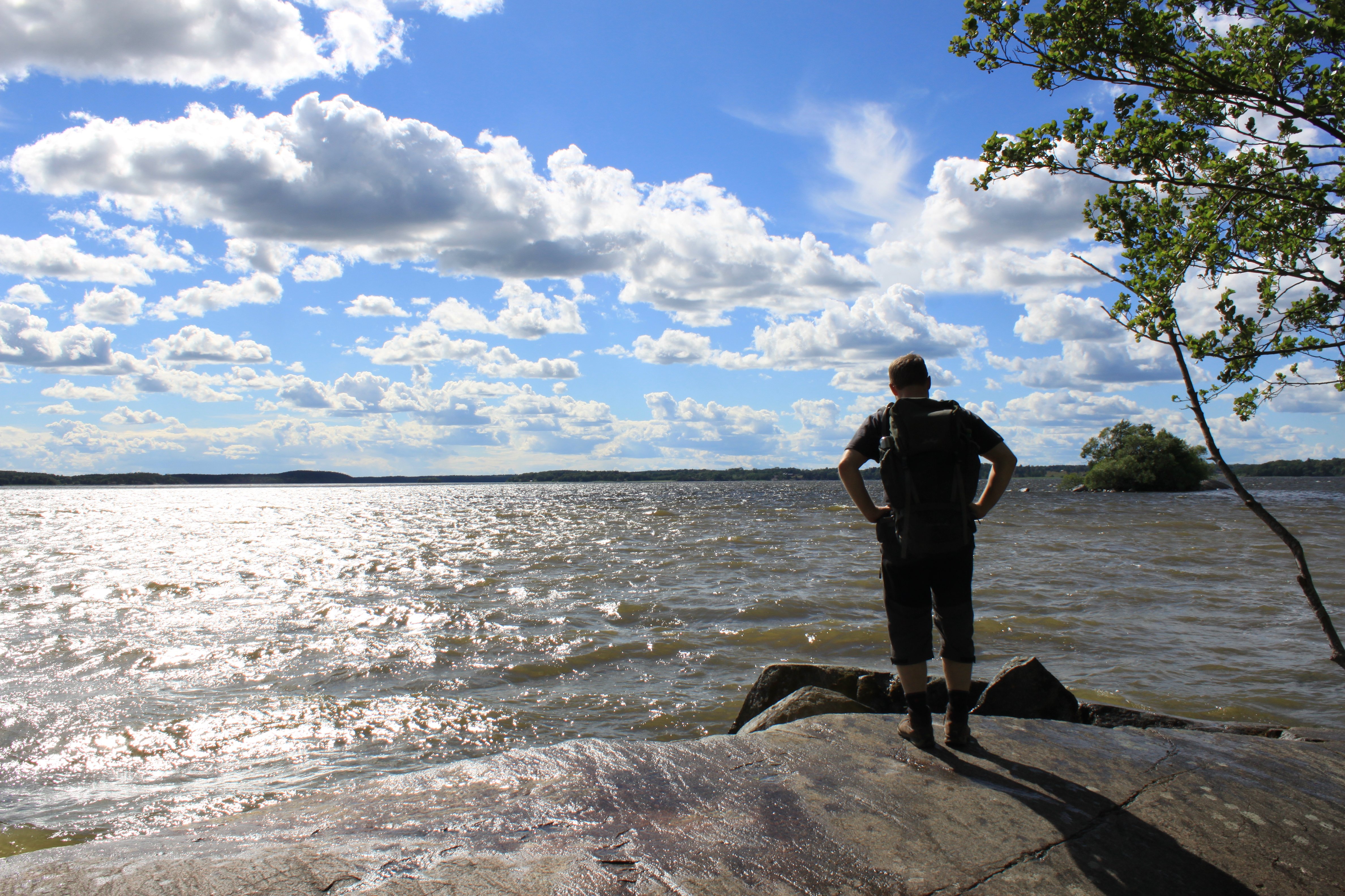 En man står på en slät klipphäll och tittar ut över vattnet. 