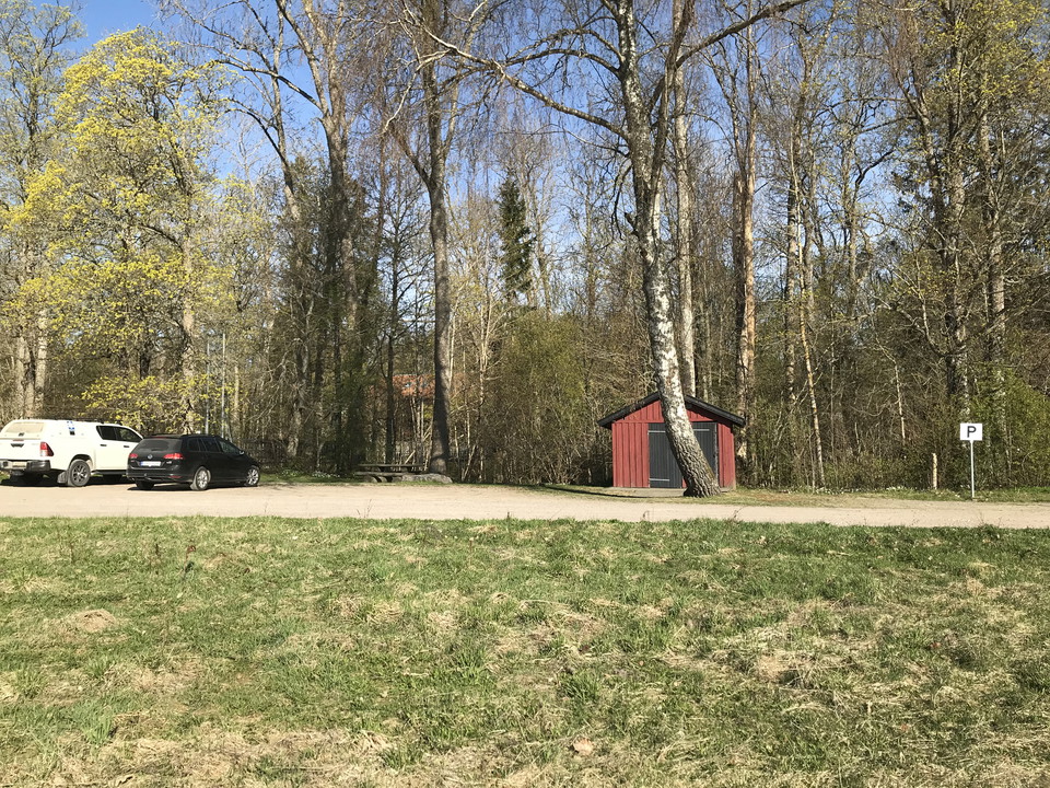 Parkeringsplats med två bilar och torrdass i mitten.