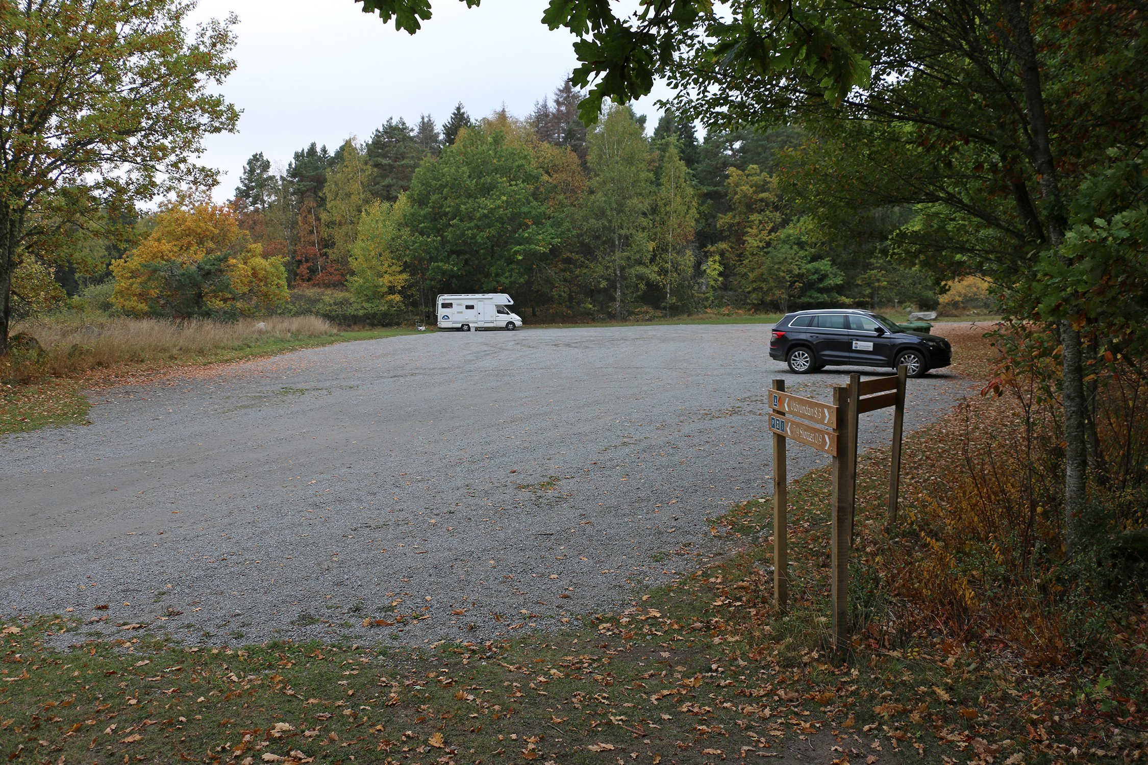 En husbil och en svart suv står parkerade en bit ifrån varandra på en fotbollsplansstor grusad yta.