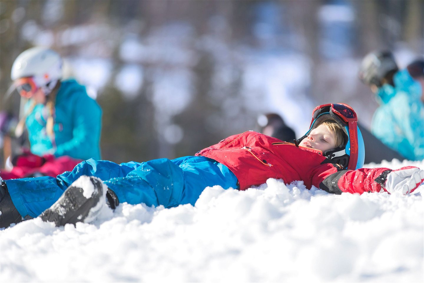 Ett barn i färgglada vinterkläder ligger i snön.