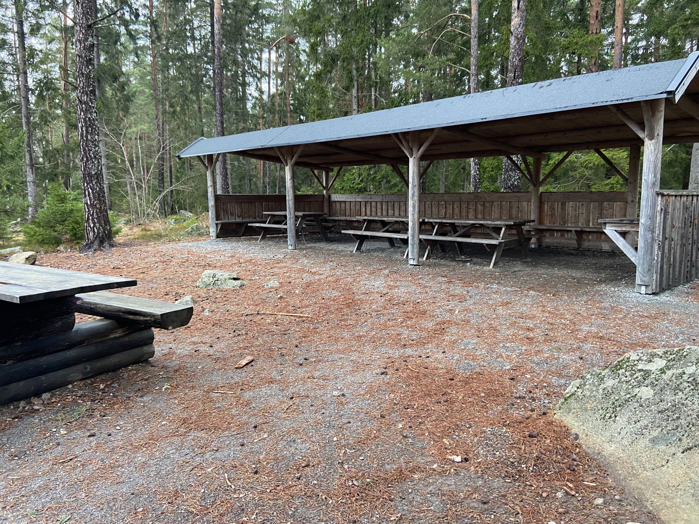 En långsträckt byggnad som består av tak, tre väggar och en öppen sida. Under taket står några bänkbord.