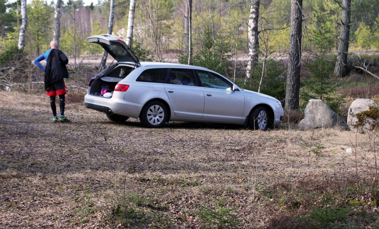 En person står bakom sin bil och klär på sig. Bilen står parkerad med bakluckan öppen.