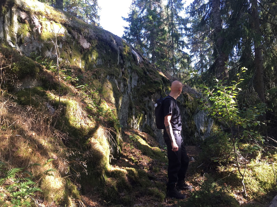 En man står bredvid en brant klippvägg som är dubbelt så hög som han är lång.