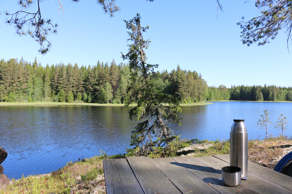 En del av ett picknickbord med en termos på, en sjö i bakgrunden.