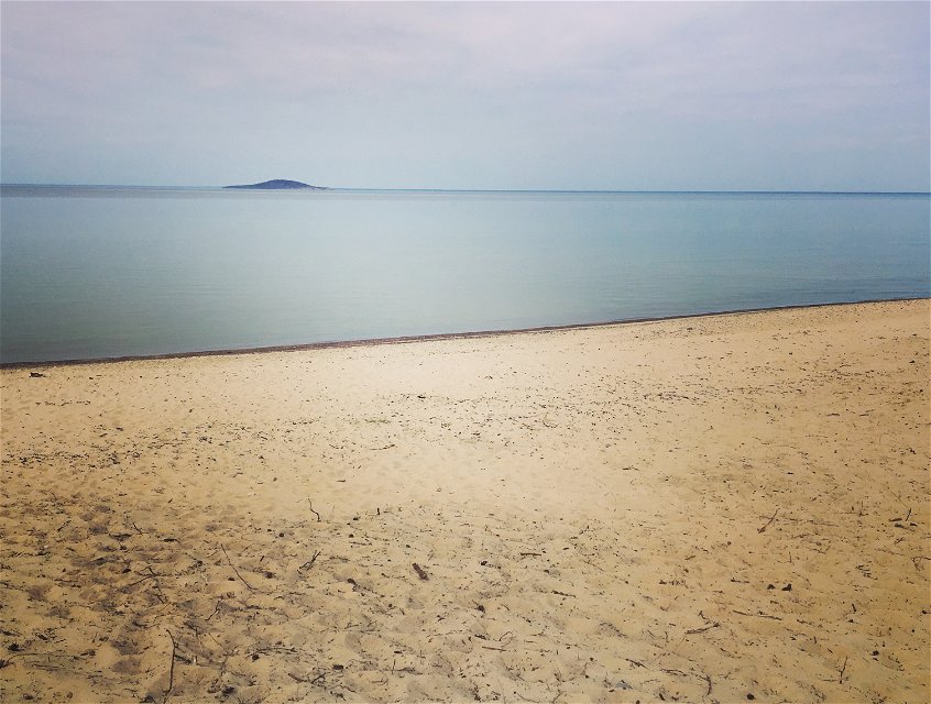 Sandstrand med stilla hav och Blå jungfrun i bakgrunden