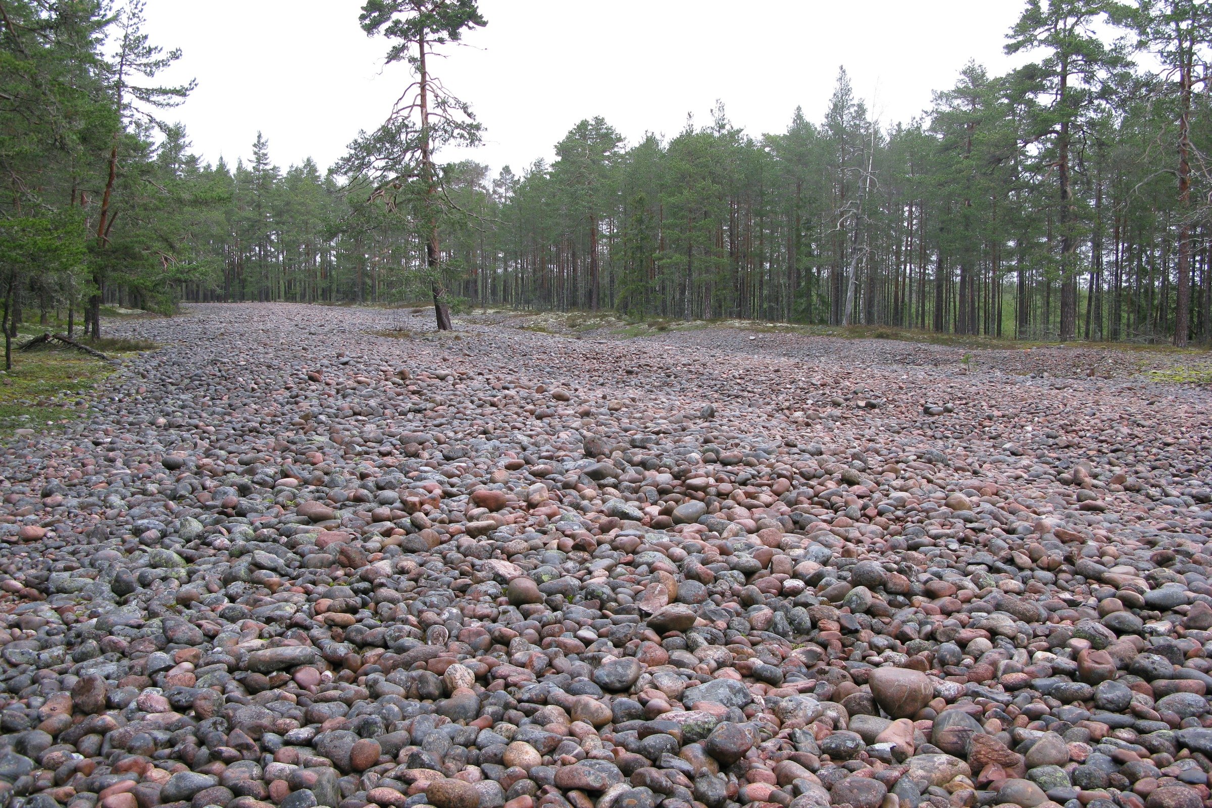 En stor öppen yta täckt av rundade stenar i olika storlekar. Stentorget är omringat av barrträd.