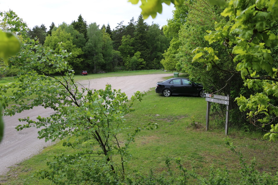 Parkering med en parkerad bil. Träskyltar visar riktningen.