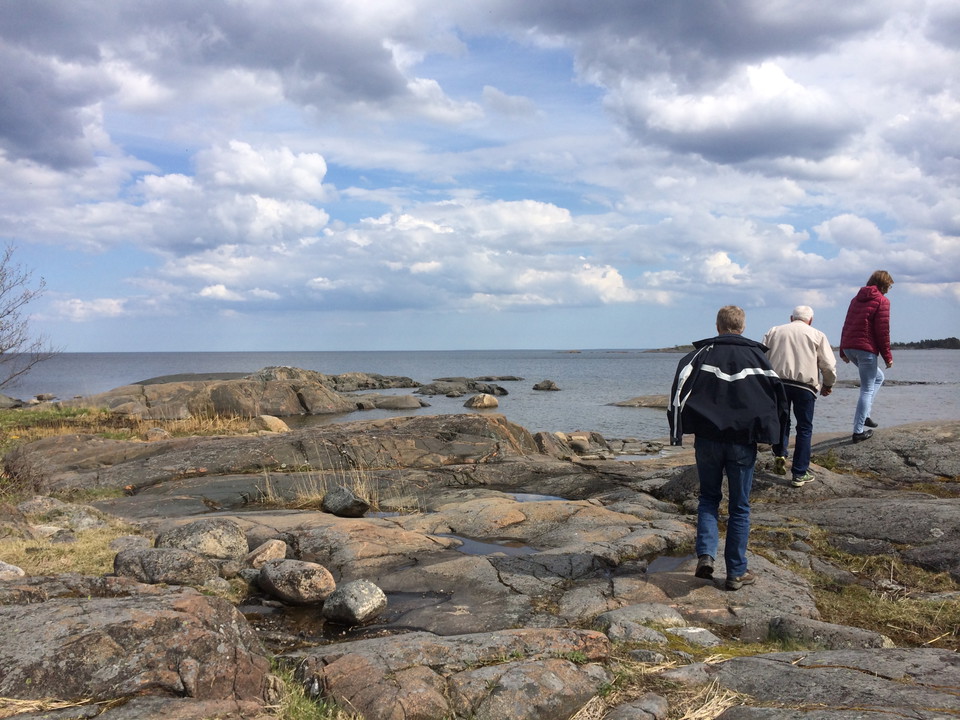 En kvinna och två män går efter varandra på en ojämn klipphäll vid havet.